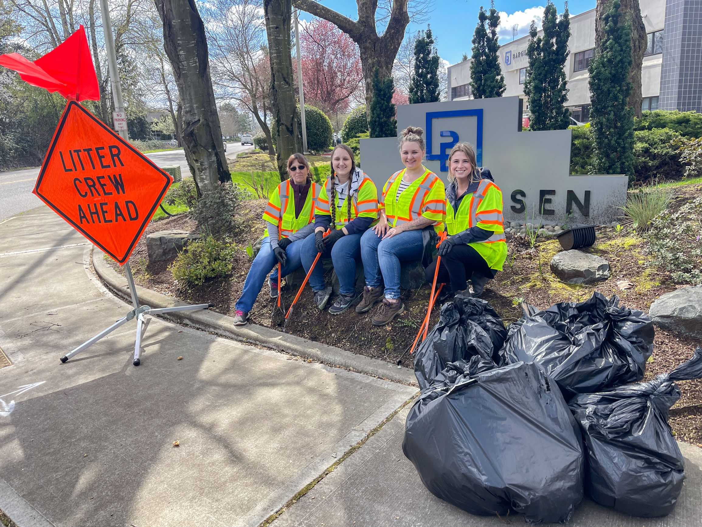Four Barghausen employees sit in front of the Barghausen sign, volunteering to pick up litter